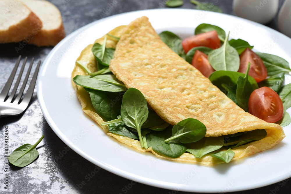 Omelet with spinach and tomatoes for breakfast in a plate on a concrete black background. Good morning.