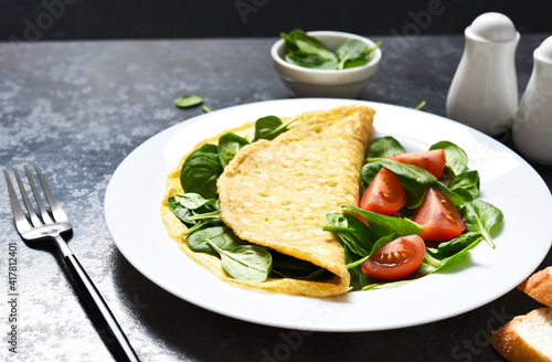 Omelet with spinach and tomatoes for breakfast in a plate on a concrete black background. Good morning.