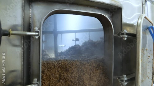 Brewer cleaning kettle in the brewery. Shoveling brewery waste and throwing into waste bag.