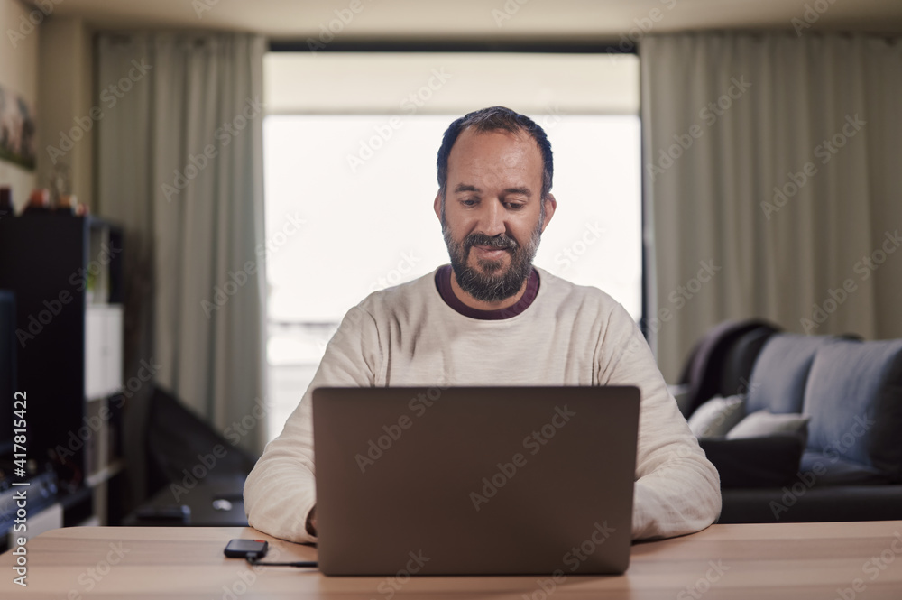 smiling middle-aged man working on laptop at home smiling middle-aged man working on laptop at home