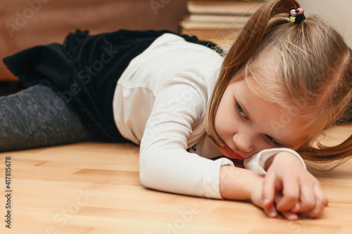 The child is bored lying on the floor. The little girl is tired of home schooling. Tired child at home on a background of books