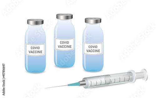 An injection syringe lying on the surface, next to three vials of coronavirus vaccine.
