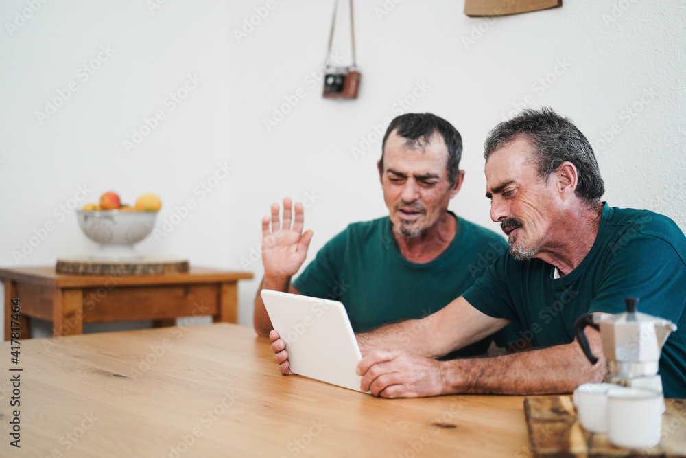 Senior twin man doing video call with tablet at home - Focus right old person face Senior twin man doing video call with tablet at home - Focus right old person face