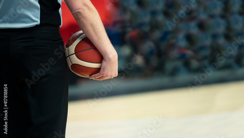 Basketball referee with ball on sport hall background.
