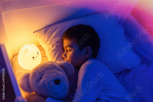 Obraz na plátně Little preschool kid boy sleeping in bed with colorful night led lamp