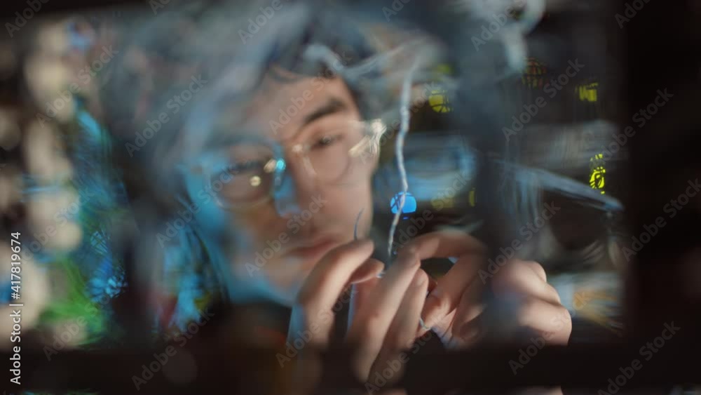 Close up of young Asian IT specialist wearing eyeglasses untangling a wire in modern server room Close up of young Asian IT specialist wearing eyeglasses untangling a wire in modern server room
