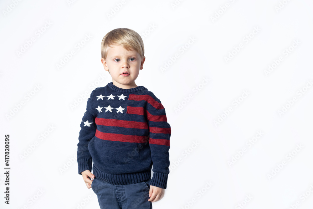 Cute boy in a sweater with an American USA flag is showing something on a white background with a copy space Cute boy in a sweater with an American USA flag is showing something on a white background with a copy space