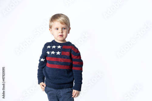 Cute boy in a sweater with an American USA flag is showing something on a white background with a copy space
