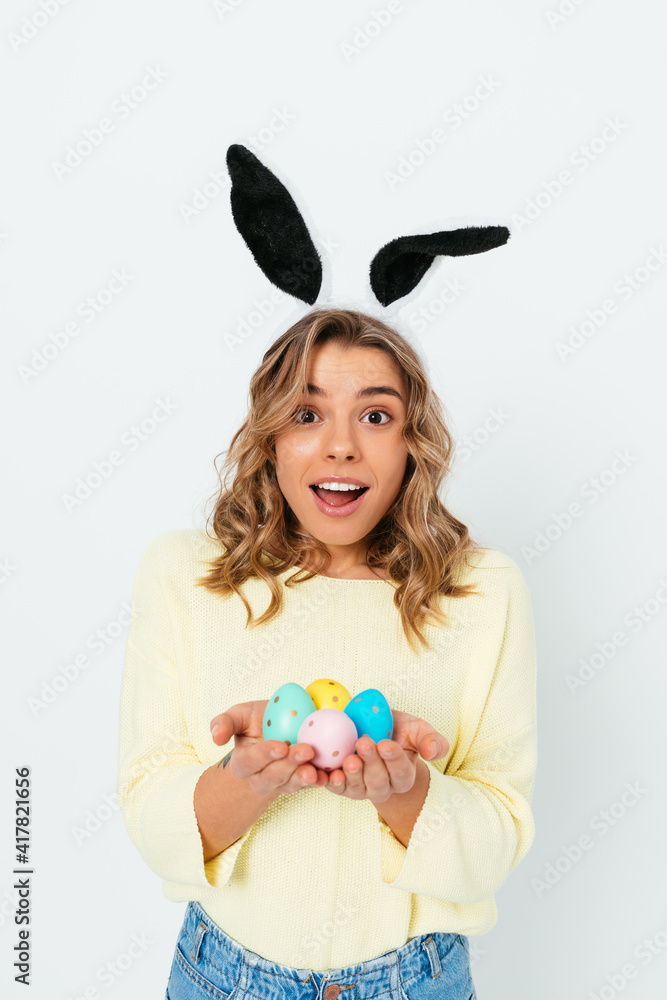 Portrait happy young woman wearing bunny ears holding colored Easter eggs Portrait happy young woman wearing bunny ears holding colored Easter eggs