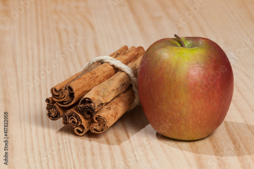 Red apple with a cinnamon stick; photo on wooden background.