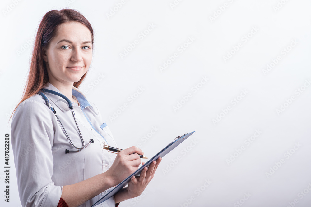 Portrait of a young female doctor in a white uniform with a folder and a pen in hands in the studio on a white background with copyspace Portrait of a young female doctor in a white uniform with a folder and a pen in hands in the studio on a white background with copyspace