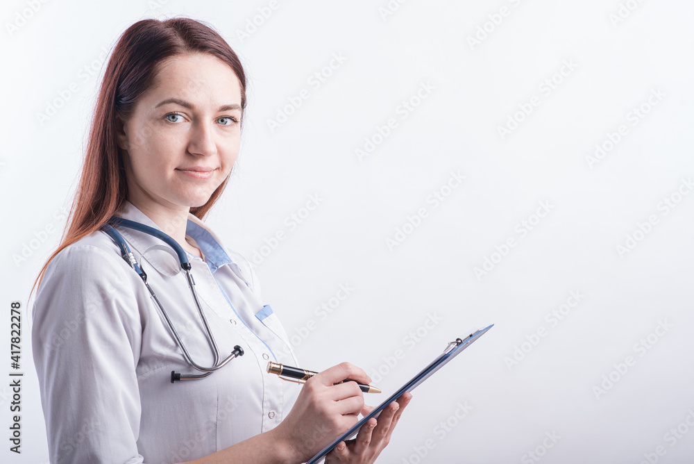 Portrait of a young female doctor in a white uniform with a folder and a pen in hands in the studio on a white background with copyspace Portrait of a young female doctor in a white uniform with a folder and a pen in hands in the studio on a white background with copyspace