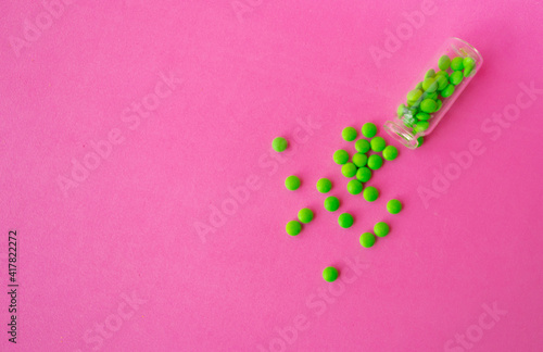 a glass ampoule is lying on the table a pile of green pills close up on a pink background