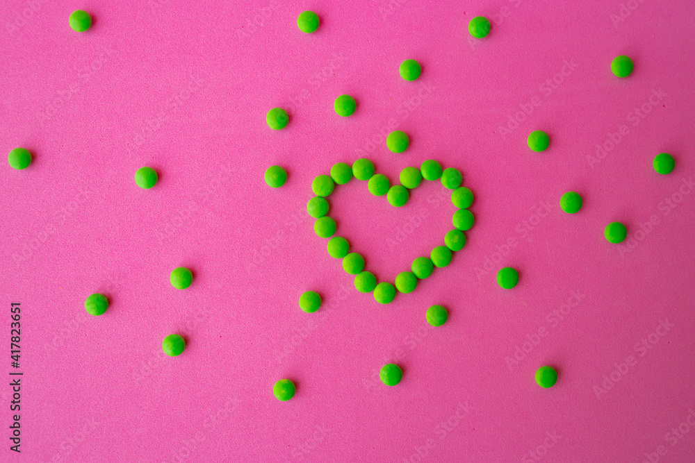 heart of green pills on a pink background, heart-shaped pills laid out on a table close-up