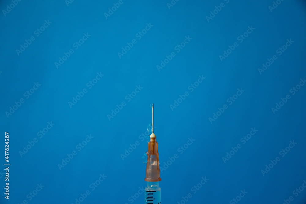 The needle of a syringe with a vaccine close-up on a blue background The needle of a syringe with a vaccine close-up on a blue background