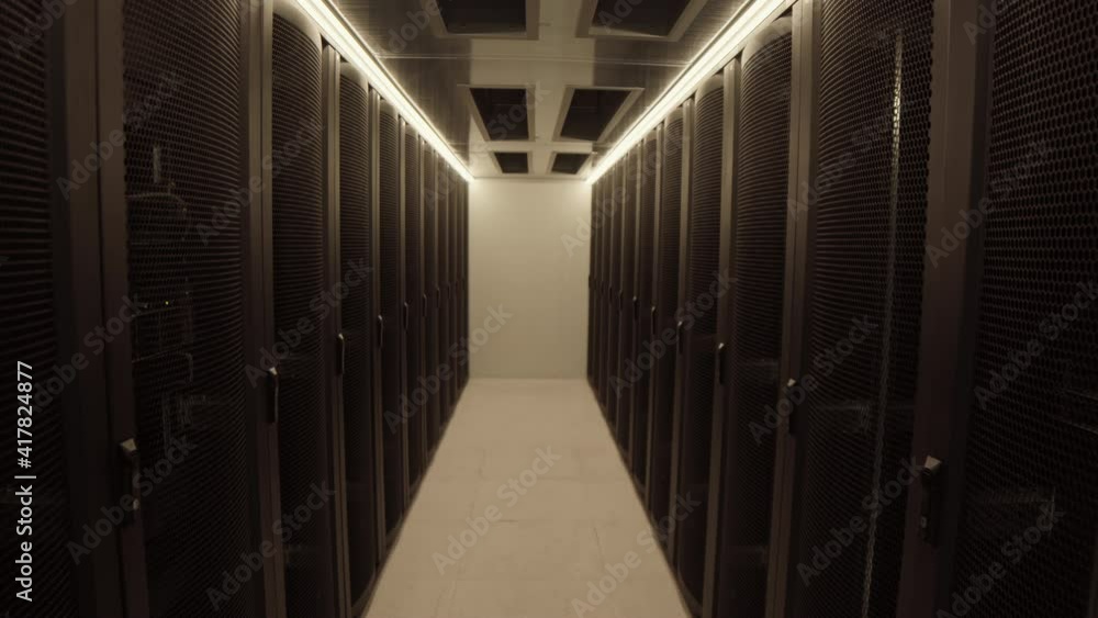 Medium shot of young Asian system administrator wearing special uniform standing in data center and programming mainframe using laptop Medium shot of young Asian system administrator wearing special uniform standing in data center and programming mainframe using laptop
