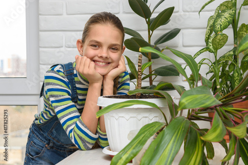 A girl examines indoor flowers and turns and looks into the frame photo