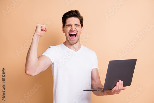 Photo of delighted handsome guy closed eyes fist up open mouth scream yeah isolated on beige color background