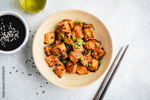 Stir fried marinated tofu with sesame seeds, soy sauce and scallions in a bowl, top view