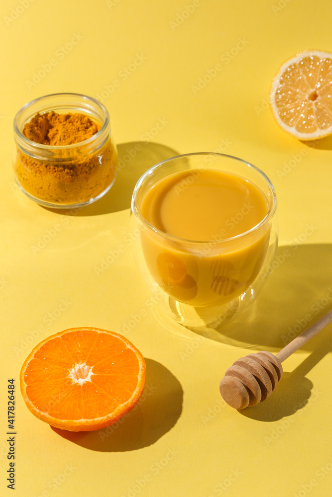 Golden milk with turmeric, Yellow drink in a thermo glass. On a bright yellow background, with orange and lemon. Hard light.