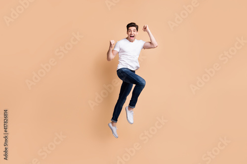 Full size profile photo of hooray brunet man jump wear t-shirt jeans sneakers isolated on beige background