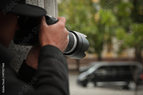 Private detective with modern camera spying on city street, closeup photo