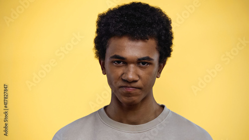 displeased african american teenage boy in sweatshirt isolated on yellow
