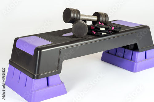 Step platform in gym with equipment for effective exercises, dumbbells and protective gloves. White background, copy space.