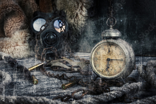Vintage clock resting on wooden surface with military gas mask and rusty chains in background