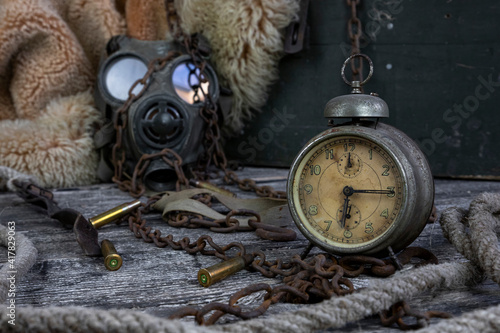 Vintage clock resting on wooden surface with military gas mask and rusty chains in background