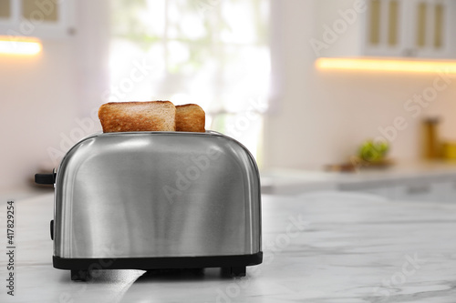 Modern toaster with slices of bread on table in kitchen. Space for text