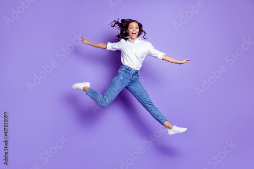 Photo of sportive active lady jump open mouth wear white shirt jeans shoes isolated violet color background