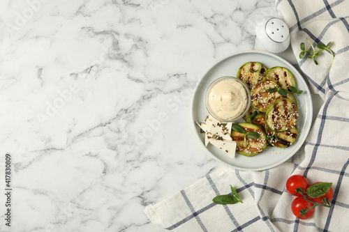 Flat lay composition with delicious grilled zucchini slices on white marble table, space for text