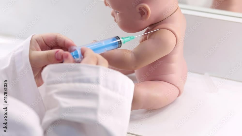 A child in a white coat plays a doctor, injects or vaccinates a doll. Vaccination through the eyes of children. A child in a white coat plays a doctor, injects or vaccinates a doll. Vaccination through the eyes of children.