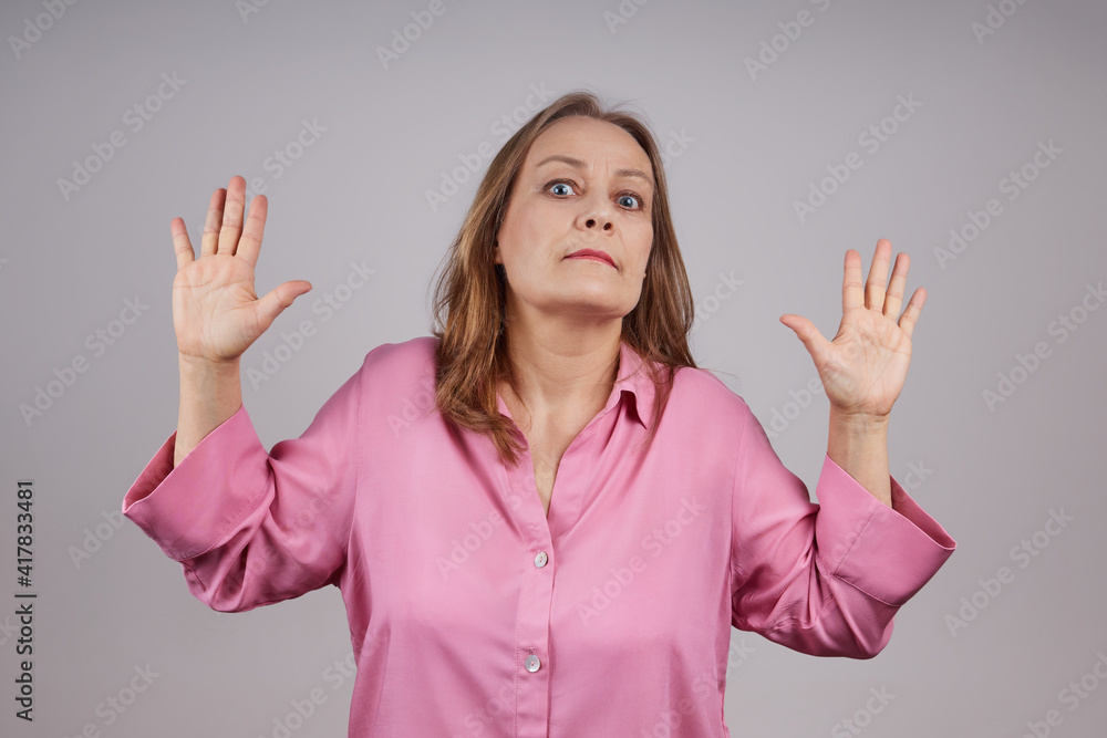 A mature woman with doubts, refusal, raised her palms. Isolated shot on gray background A mature woman with doubts, refusal, raised her palms. Isolated shot on gray background