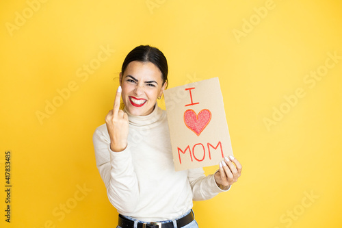 Beautiful woman celebrating mothers day holding poster love mom message showing middle finger doing fuck you bad expression, provocation and rude attitude. screaming excited