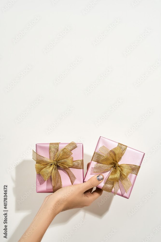 Happy Womens day. Vertical shot of a female hand holding two small wrapped gift boxes with golden bows against white background Happy Womens day. Vertical shot of a female hand holding two small wrapped gift boxes with golden bows against white background