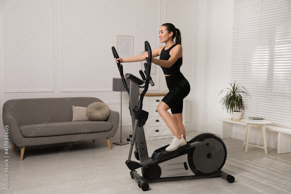 Fototapeta premium Happy young woman training on elliptical machine at home