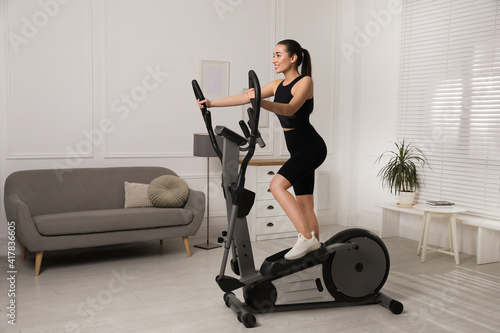 Happy young woman training on elliptical machine at home photo