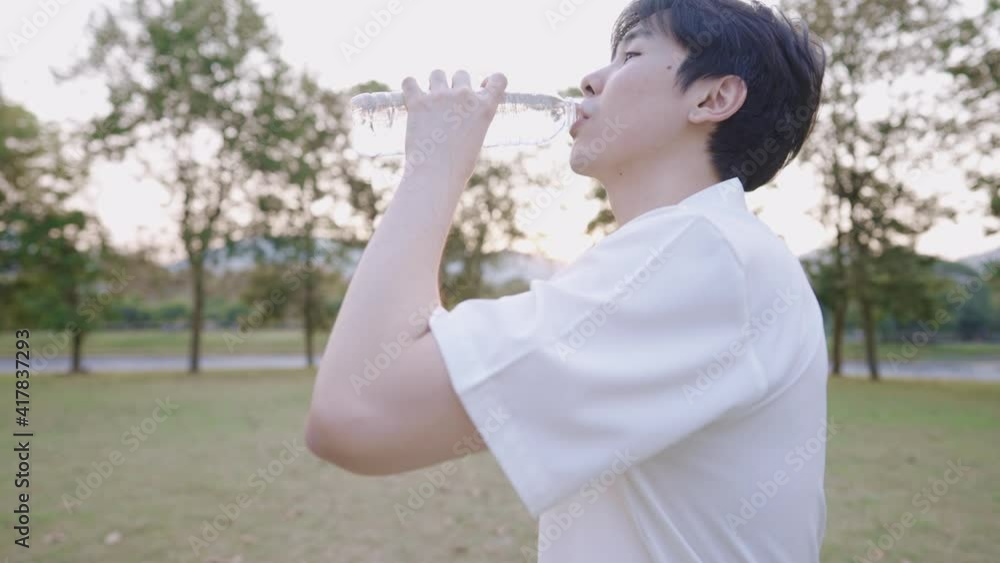 young handsome asian man drinking water while relaxing at outdoor park with sunsetting in distance, feeling fresh with healthy skin moisture concept, rehydration mineral vitamin water, side view shot young handsome asian man drinking water while relaxing at outdoor park with sunsetting in distance, feeling fresh with healthy skin moisture concept, rehydration mineral vitamin water, side view shot
