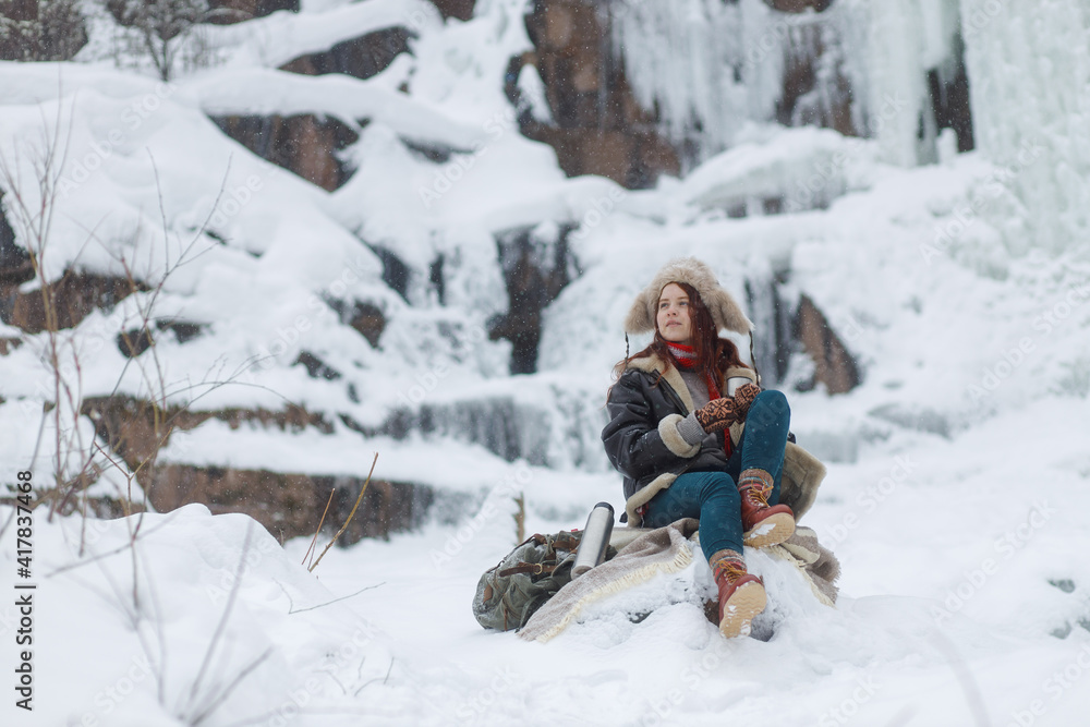 Fototapeta premium Winter outdoor recreation. Young woman drinks hot tea from thermos