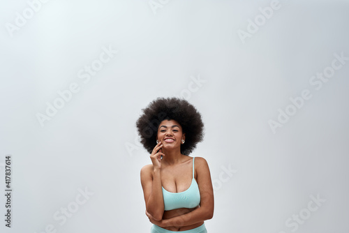 Excited voluptuous young woman with afro hair style wearing blue underwear smiling at camera  posing isolated over light background