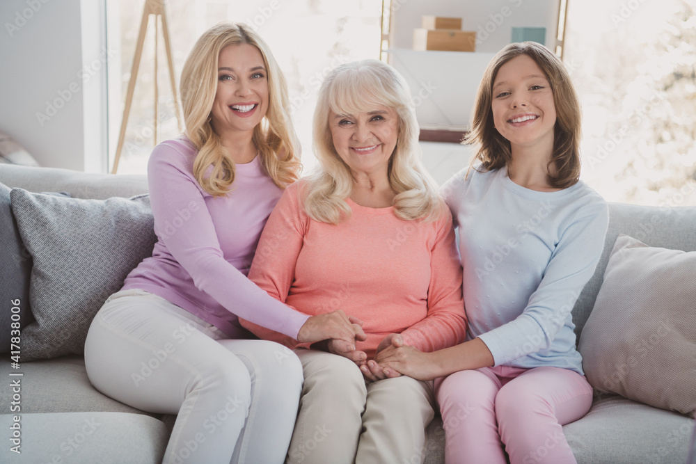 Photo of mother grandmother and daughter sit sofa hold hands family picture generation indoors inside house home