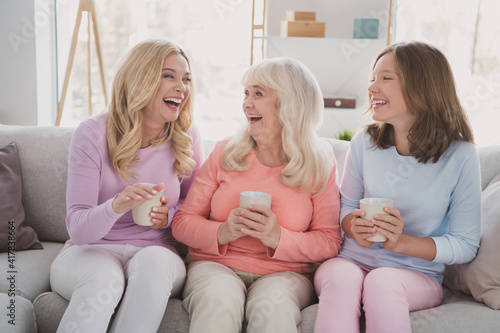 Photo of positive happy family women sit sofa drink coffee weekend relax smile indoors inside house