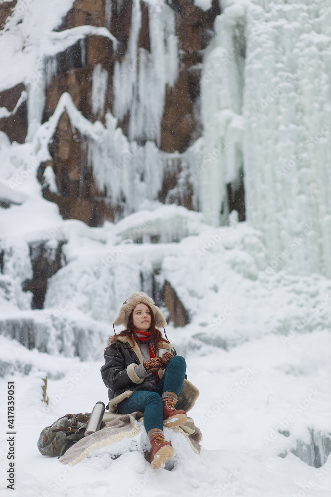 Fototapeta premium Winter outdoor recreation. Young woman drinks hot tea from thermos