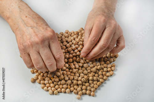 An elderly woman is sorting through the seeds of garbanzo beans on a white background. Isolated