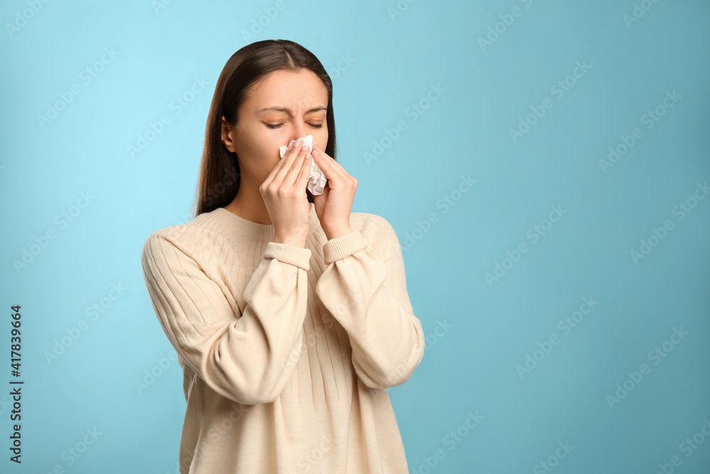 Young woman with tissue suffering from runny nose on light blue background. Space for text Young woman with tissue suffering from runny nose on light blue background. Space for text