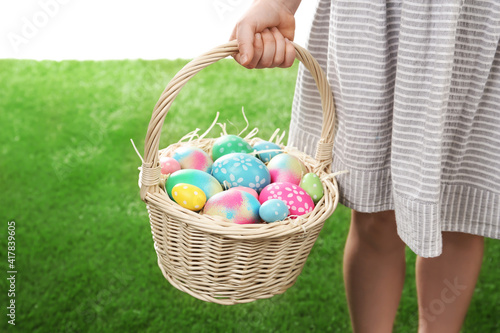 Little girl with basket full of Easter eggs on green grass against white background, closeup photo