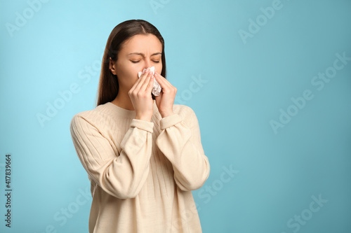 Fotografie Young woman with tissue suffering from runny nose on light blue background