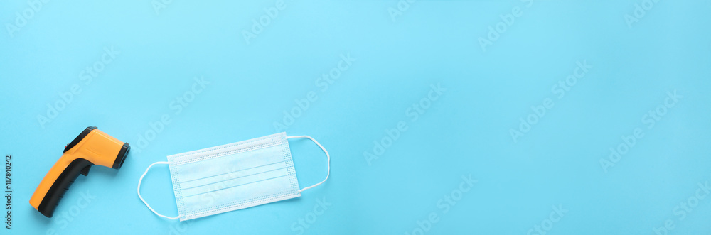 Infrared thermometer and medical mask on light blue background, flat lay with space for text. Checking temperature during Covid-19 pandemic Infrared thermometer and medical mask on light blue background, flat lay with space for text. Checking temperature during Covid-19 pandemic